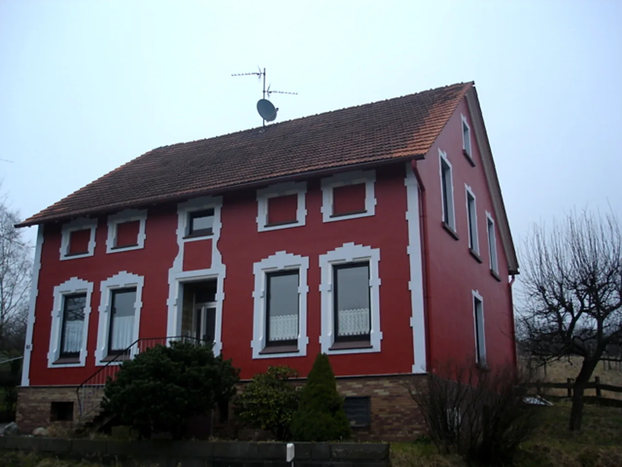 Rot gestrichene Fassade eines Wohnhauses mit weiß abgesetzten Fensterfaschen